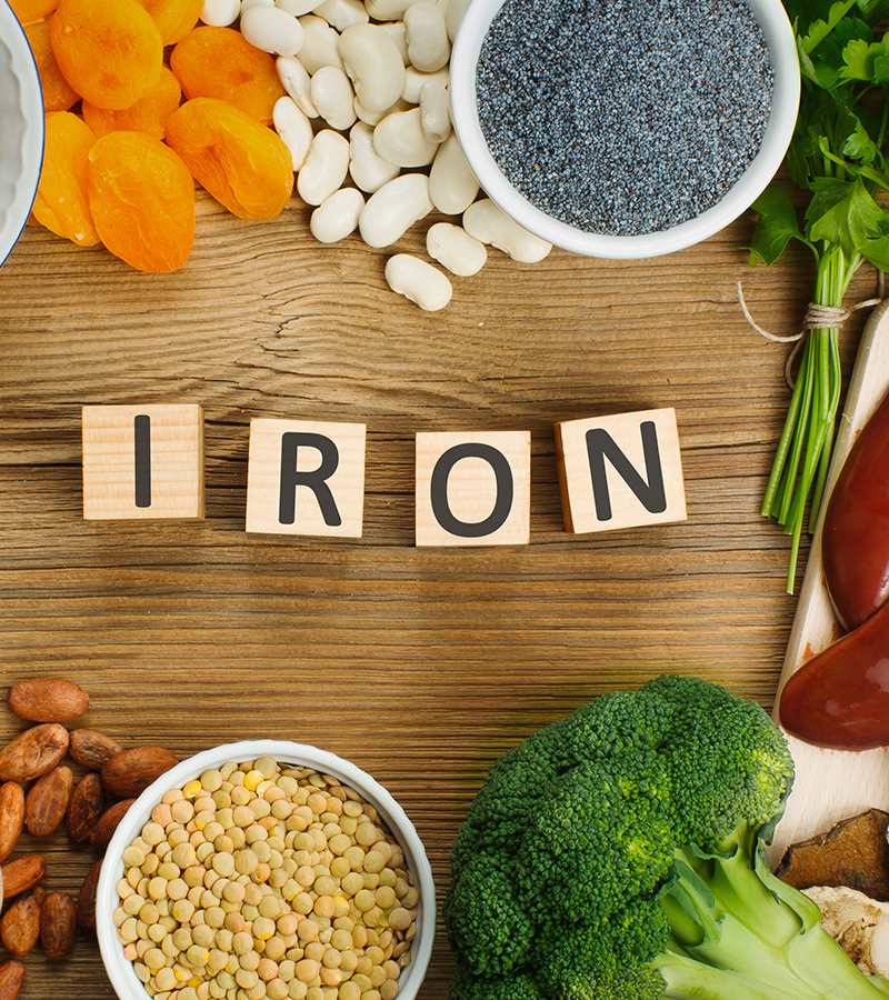 Assortment of high in Iron sources on wooden background: liver, beef, raisins, cashew, buckwheat, spinach, tomatoes, potatoes, dark chocolate, pumpkin seeds, lentil, broccoli. Top view.