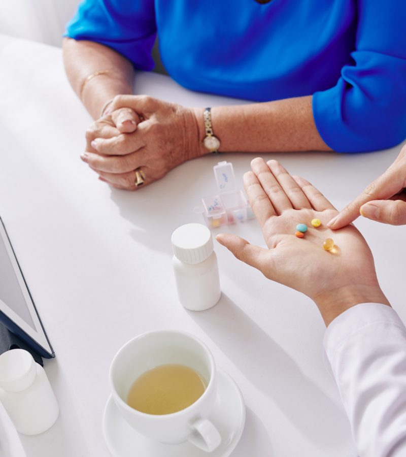 Doctor pointing at pills in her hand when explaining aged woman hany many supplements she should take daily