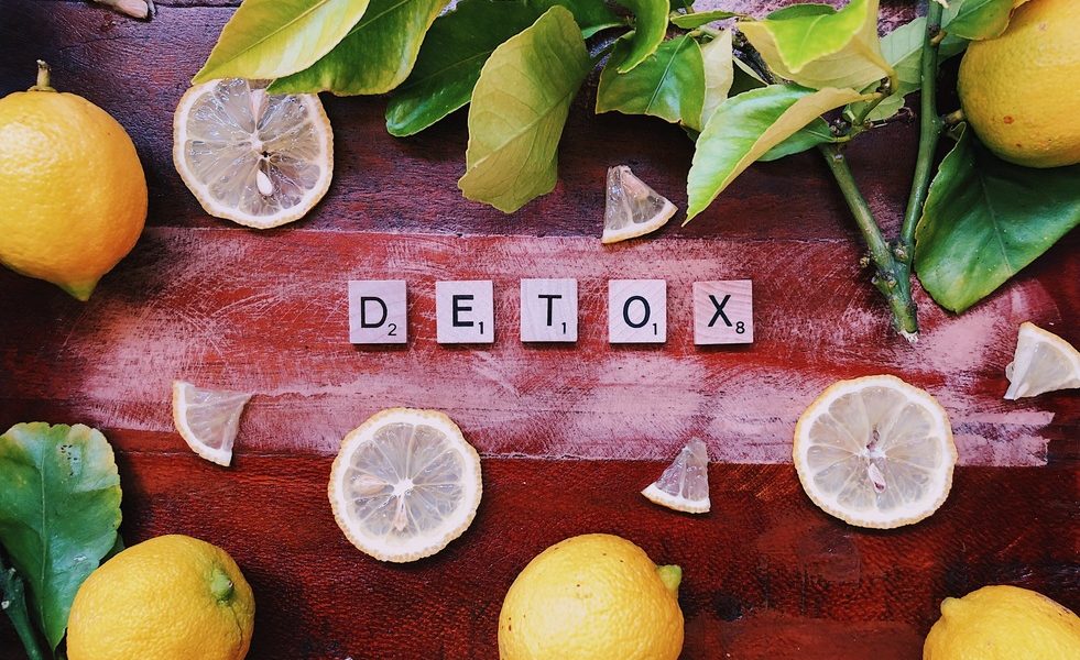 DETOX written in scrabble letters on a wood table with lemons