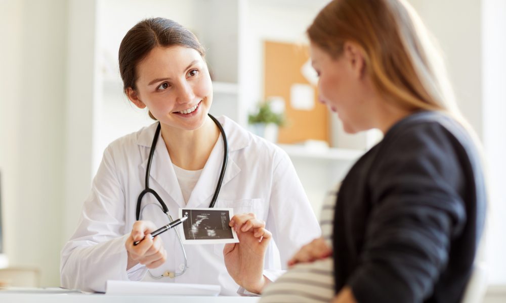 smiling onstetrician showing ultrasound scan of baby to pregnant woman visiting doctor