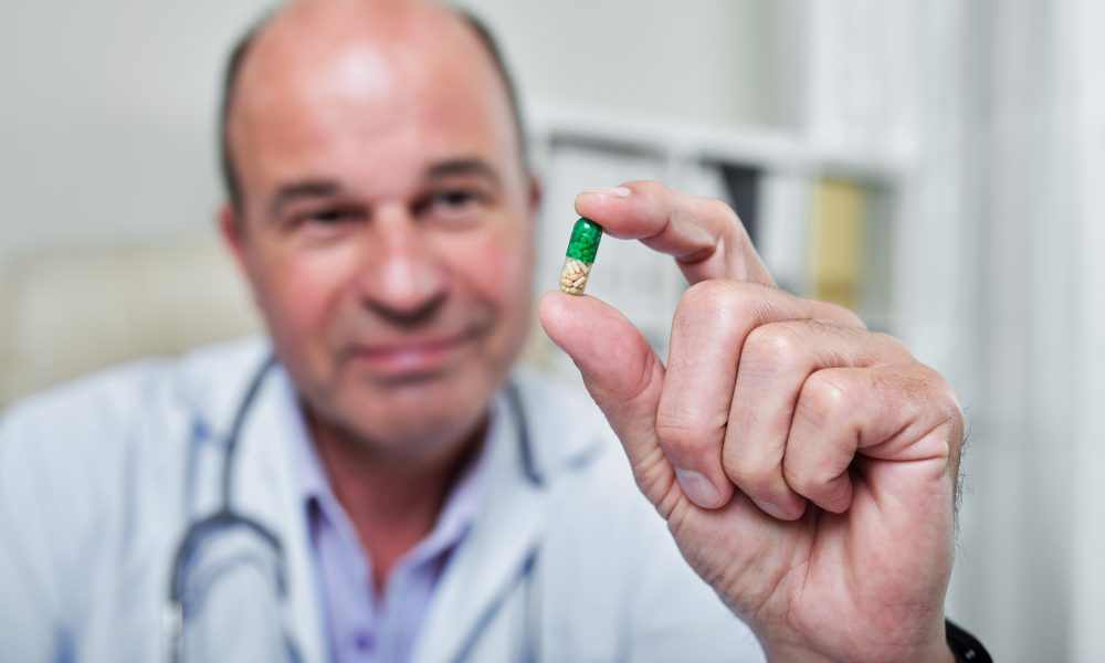 Green and yellow supplement pill in hand of general practitioner, selective focus