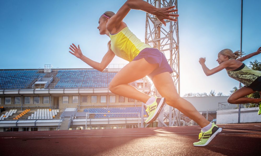 two female sprinter athletes running on the treadmill race during training in the athletics stadium.