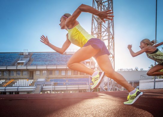 two female sprinter athletes running on the treadmill race during training in the athletics stadium.