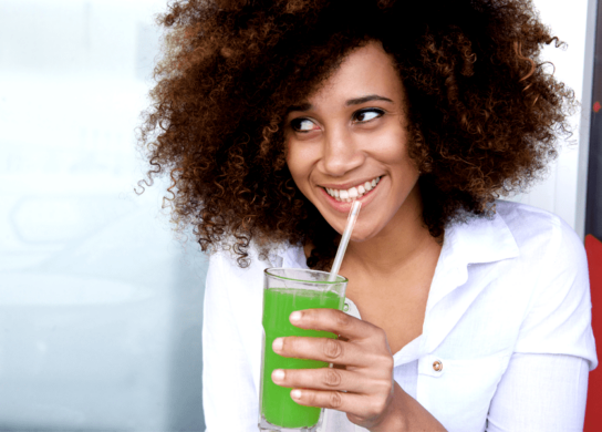 A woman drinking a green smoothie and smiling.