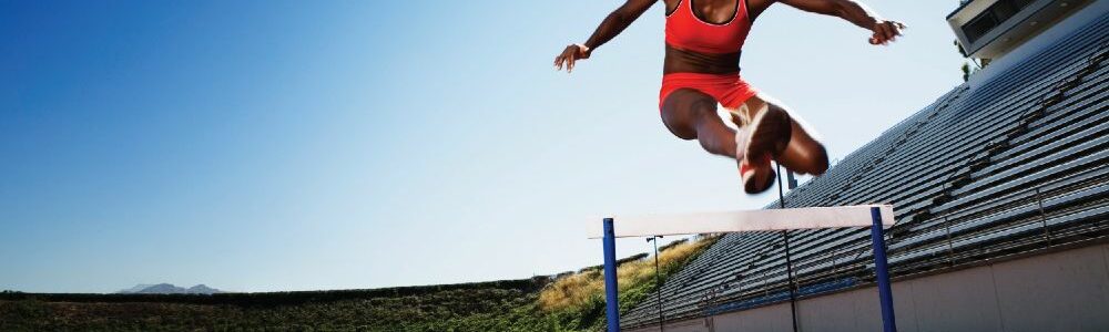 A woman jumping over a hurdle demonstrating sports performance exercise.