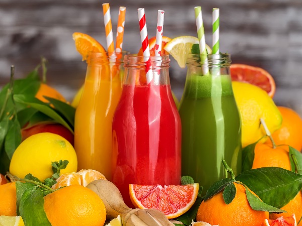 Three (3) glass bottles with colorful straws filled with fruit juice and various lemons, oranges, and grapefruit sitting on a table.