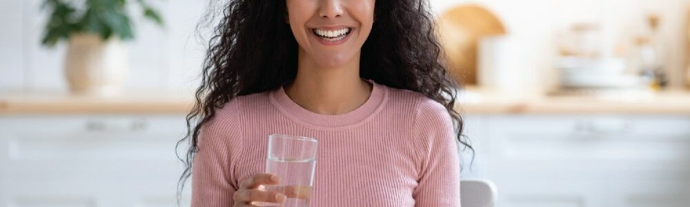 A beautiful woman smiling, getting ready to take a supplement with a glass of water